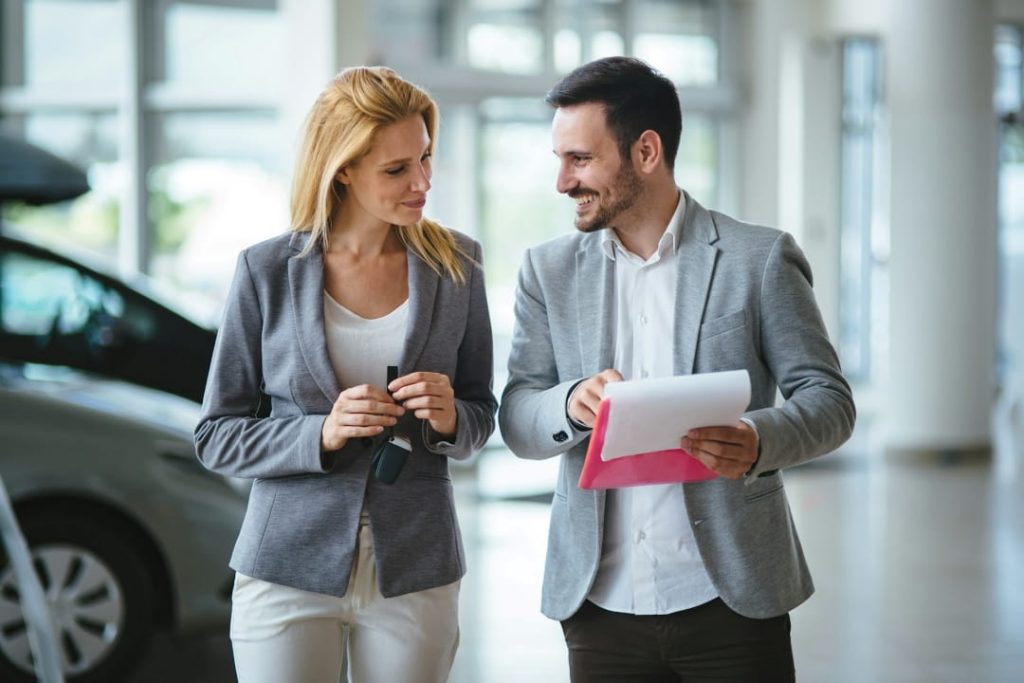 two people in a car dealership discussing paperwork