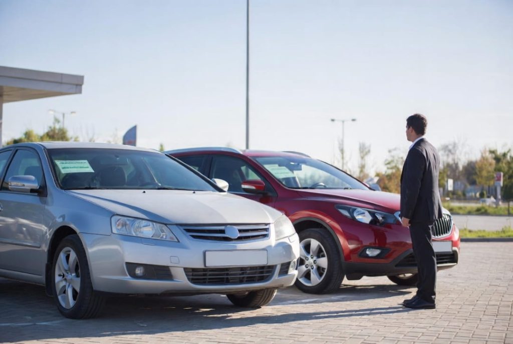 car dealer inspecting two vehicles parked on a dealership lot